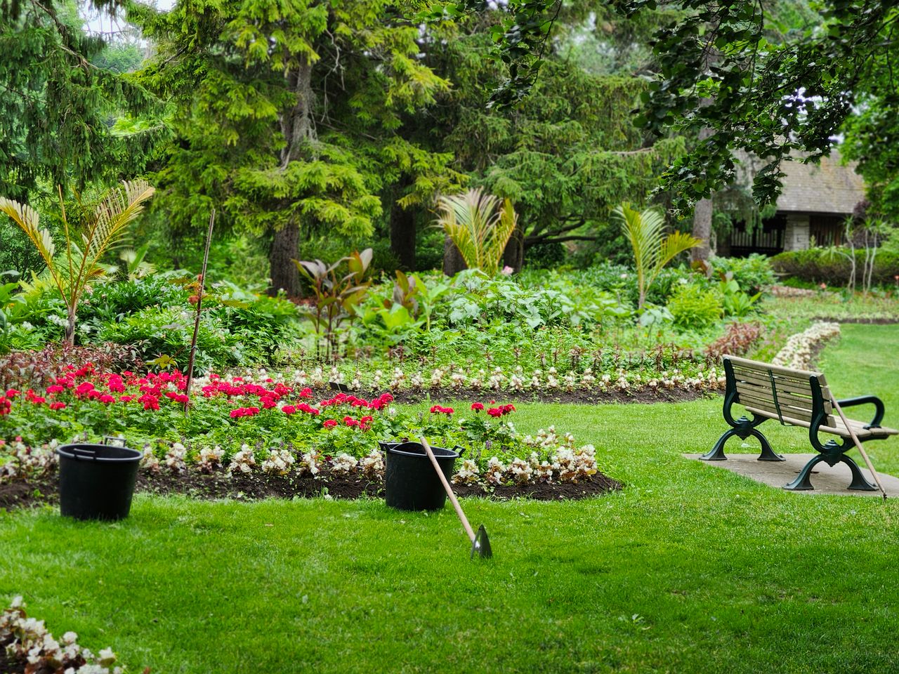 about-us-img Tranquil park scene featuring lush greenery, a flower garden, and an empty bench.